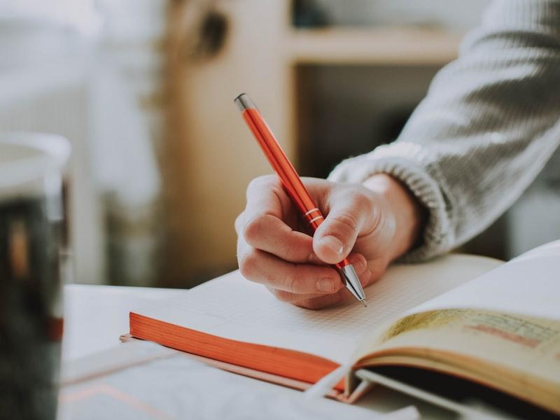 Person holding a pen while writing in a journal